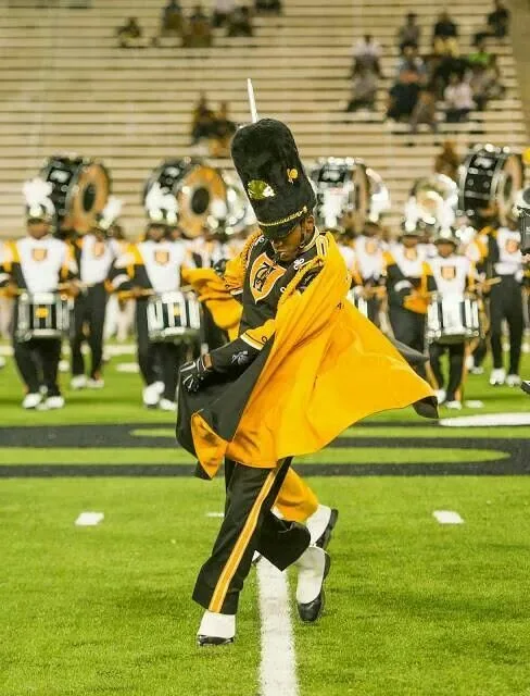A Mighty Marching Hornets drum major dances in a flowing gold cape in front of the drumline